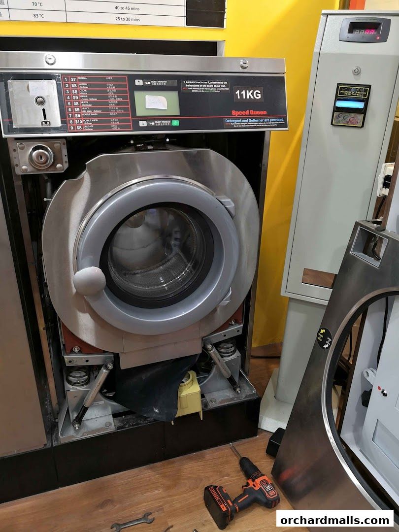 A commercial washing machine with its front panel open, showing internal components and tools nearby.