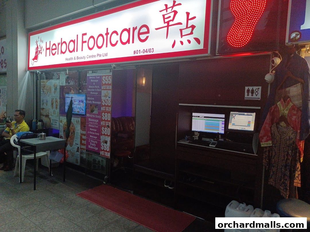 The storefront of Herbal Footcare, displaying services and prices, with a man sitting outside.