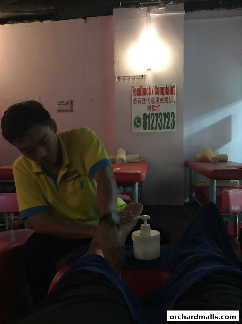 A person receives a foot massage from a therapist in a dimly lit room.