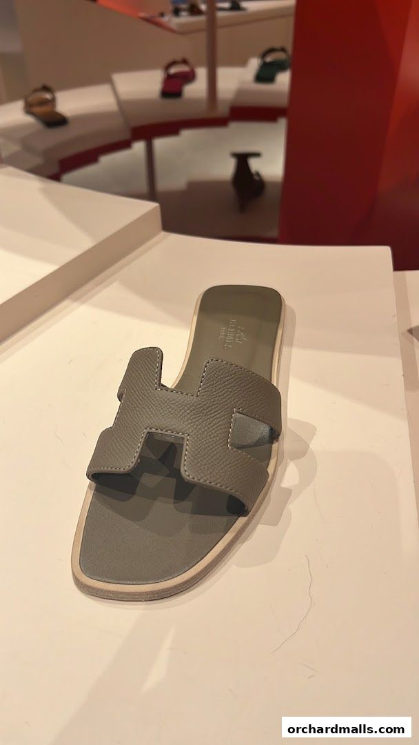 A close-up of a grey Hermès 'H' slide sandal on display.