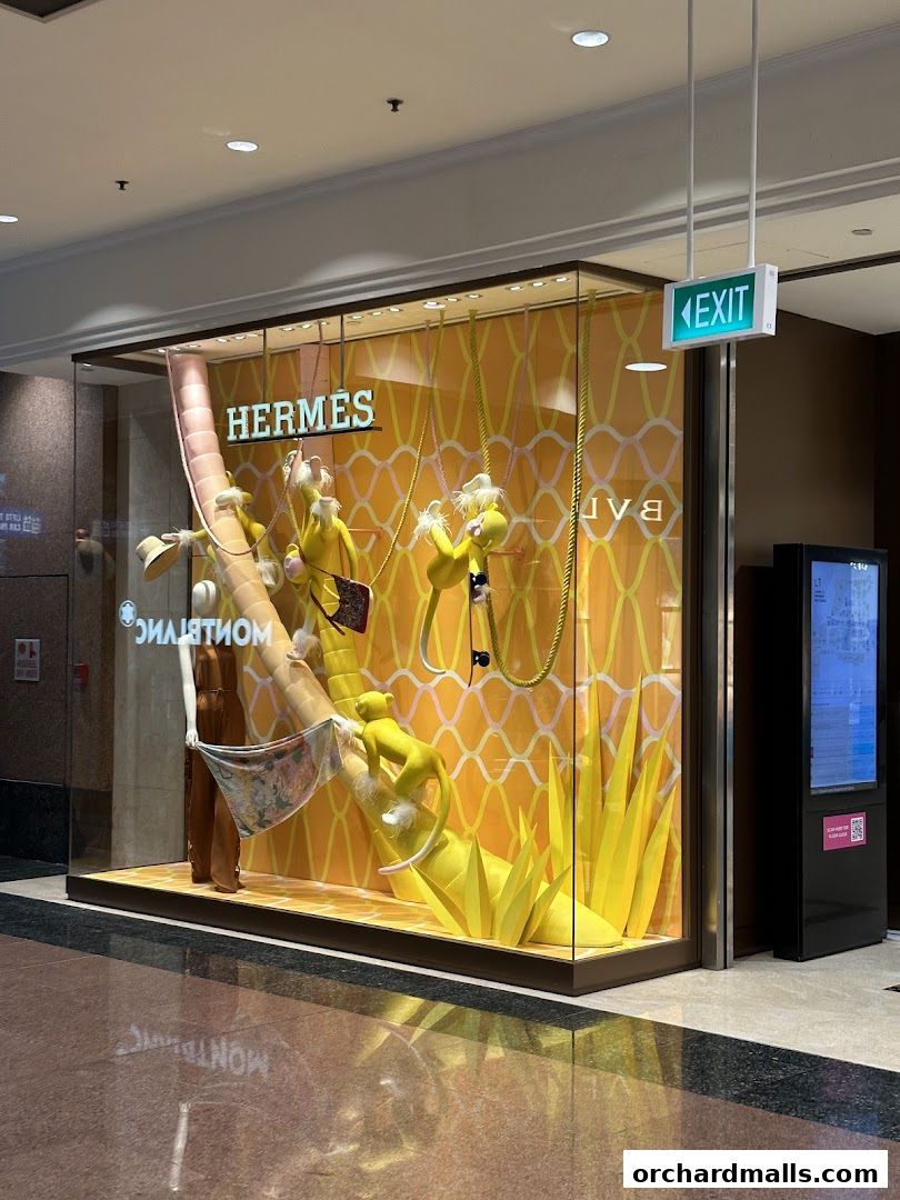 Hermès Singapore Takashimaya shop window display with playful yellow figures and a vibrant orange backdrop.