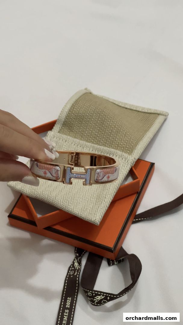 A hand displays a decorative Hermès bracelet with an orange box and ribbon.