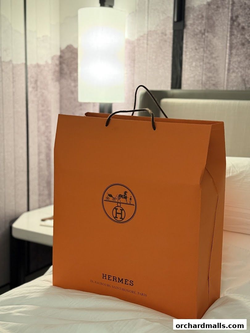 An orange Hermès shopping bag with the iconic logo and address on a bed.