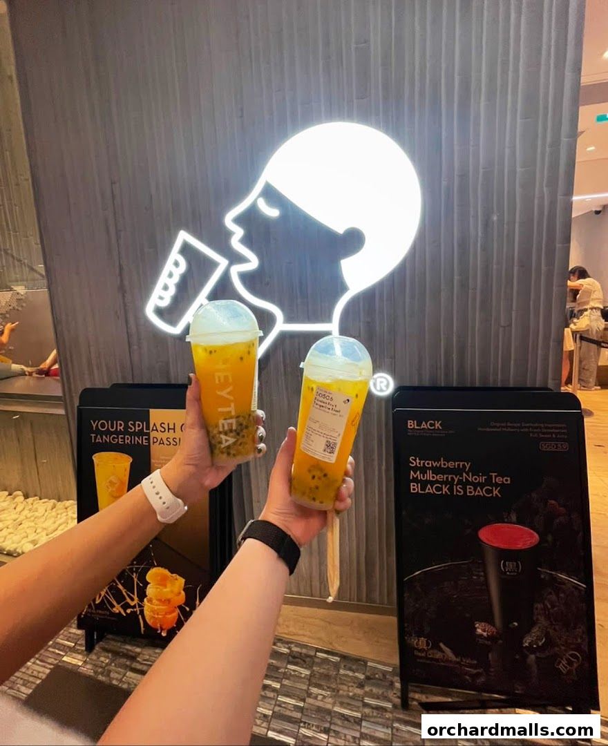 Two people holding HEYTEA drinks in front of the shop's neon logo.