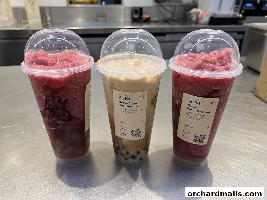 Three takeaway drinks from HEYTEA, including a brown sugar boba milk tea and two grape slushies.