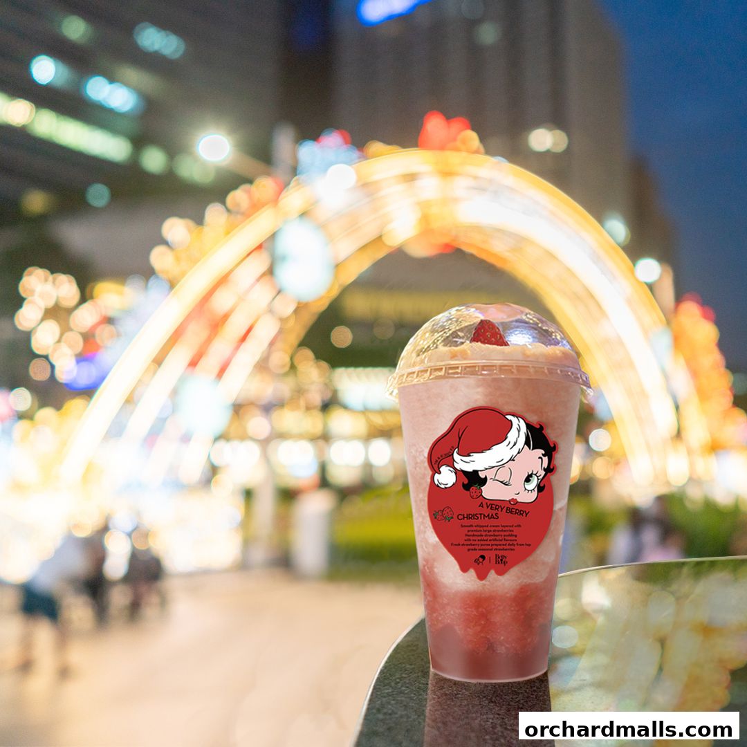 A festive strawberry drink with a Betty Boop Christmas sticker in front of blurred holiday lights.