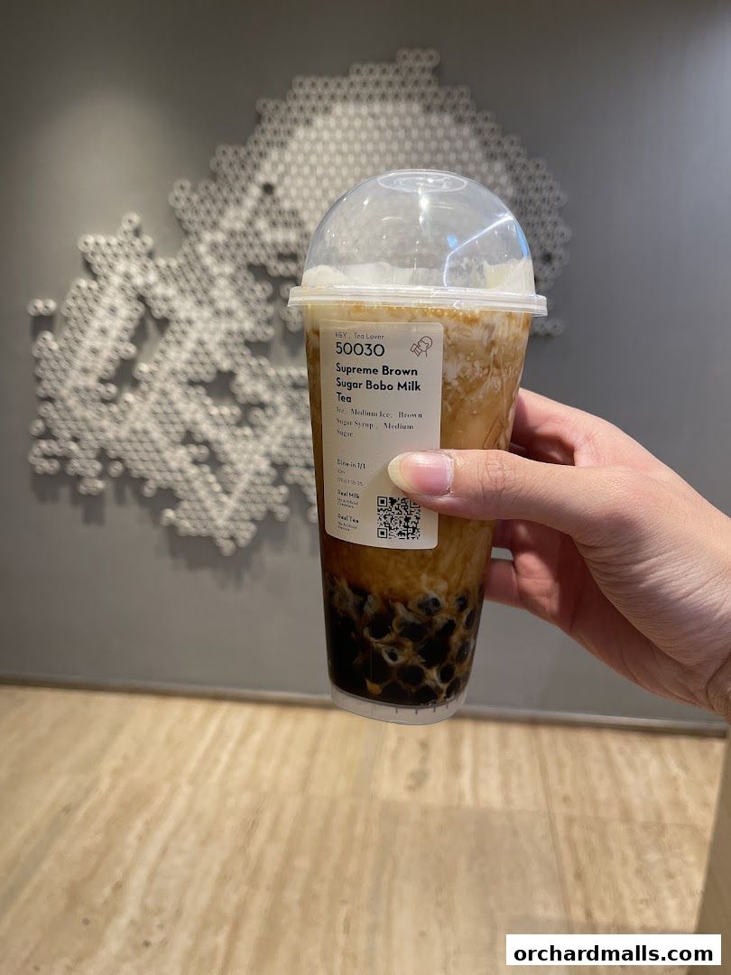 A hand holds a bubble tea with brown sugar and boba pearls against a textured wall.