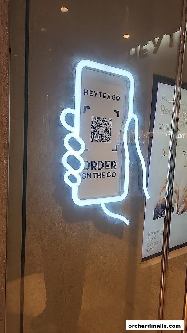 Neon sign for HEYTEA GO showing a hand holding a phone with a QR code for ordering.