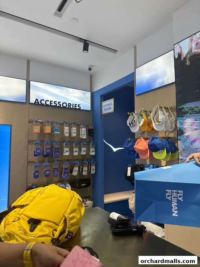 Interior of a HOKA store with accessories and caps displayed, and a customer holding a shopping bag.