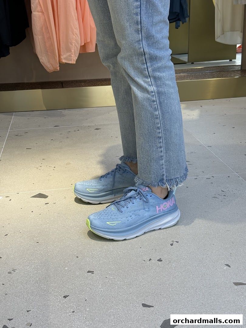 A person wearing light blue Hoka running shoes and distressed jeans inside a store.