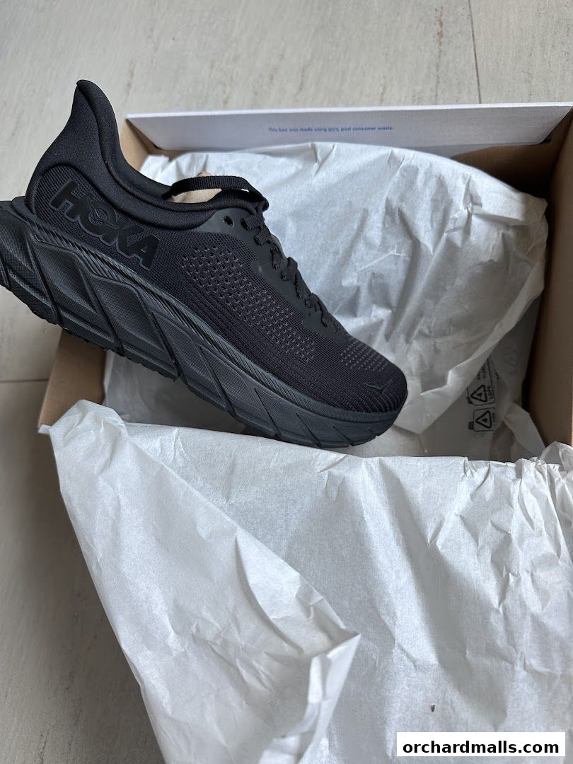 A black Hoka running shoe is presented in its open box with white tissue paper.