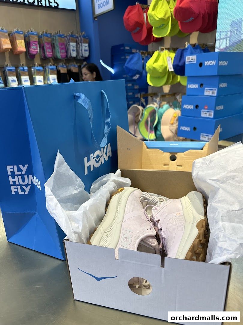 HOKA shoes in a box with a shopping bag and accessories in the background.