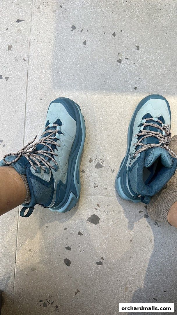 A person wearing blue Hoka hiking boots on a speckled gray floor.