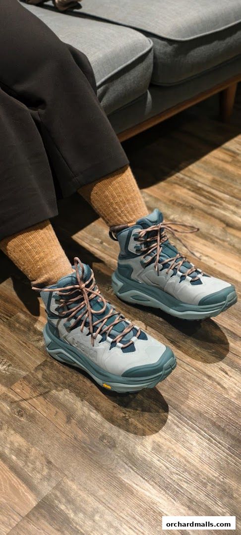 A person wearing Hoka hiking boots and brown socks sits on a grey couch.