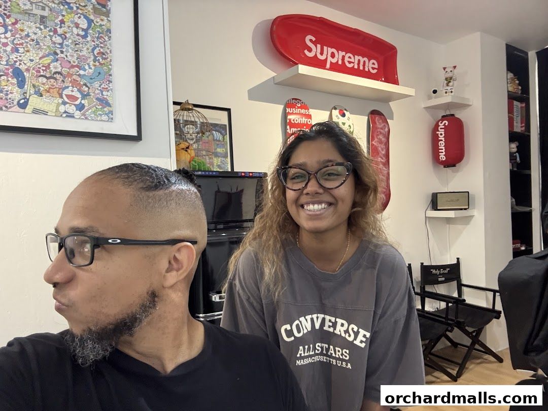 Two people smiling in a barbershop with Supreme decor and artwork.