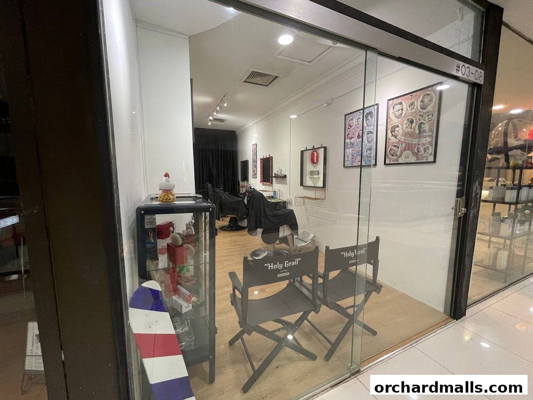 Interior of Holy Grail Barbershop with barber chairs, posters, and display cases visible through the glass.
