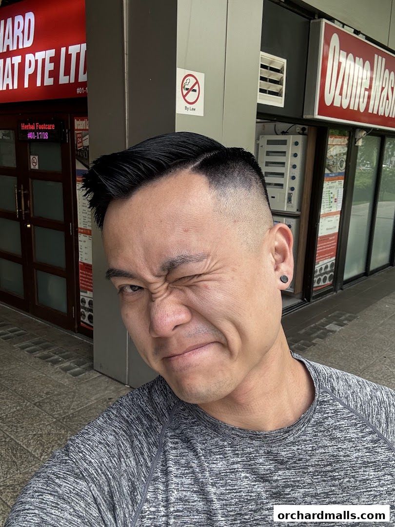 A man with a fresh haircut poses in front of a barbershop and a laundry service.
