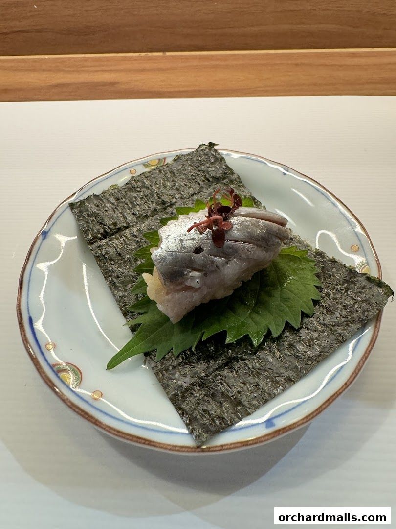 A delicate Japanese dish featuring fish, nori, and shiso leaf on a decorative plate.