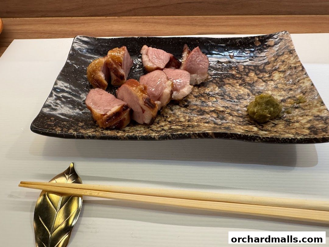 Slices of grilled duck with a side of green paste served on a decorative plate with chopsticks.