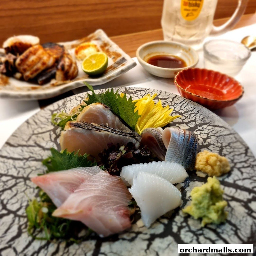 A close-up of a sashimi platter with various fish, squid, wasabi, and a drink.