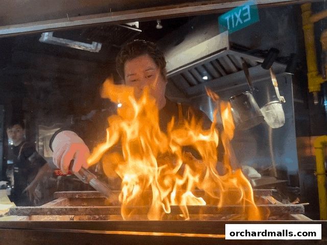 A chef prepares food over an open flame in a restaurant kitchen.