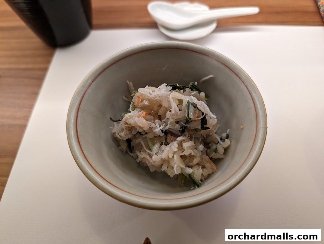 A close-up of a small bowl filled with rice and shredded ingredients, served with a spoon.