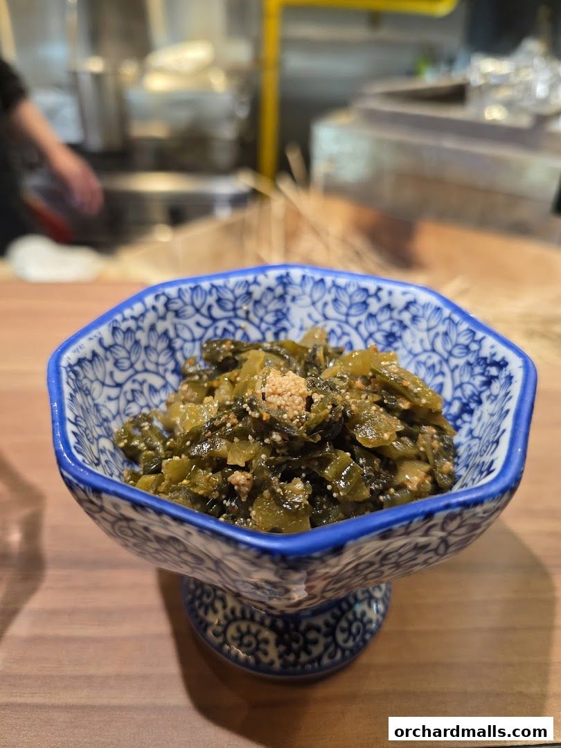 A close-up of a decorative bowl filled with a savory, chopped green dish, likely a Japanese appetizer.