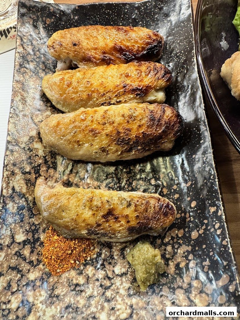 Four grilled chicken wings served with a side of spice mix and wasabi.