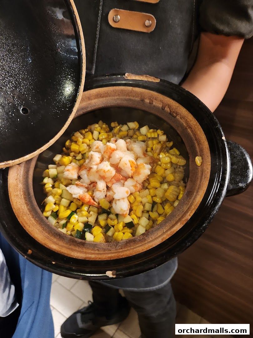 A person holding a pot of steaming corn, zucchini, and shrimp.