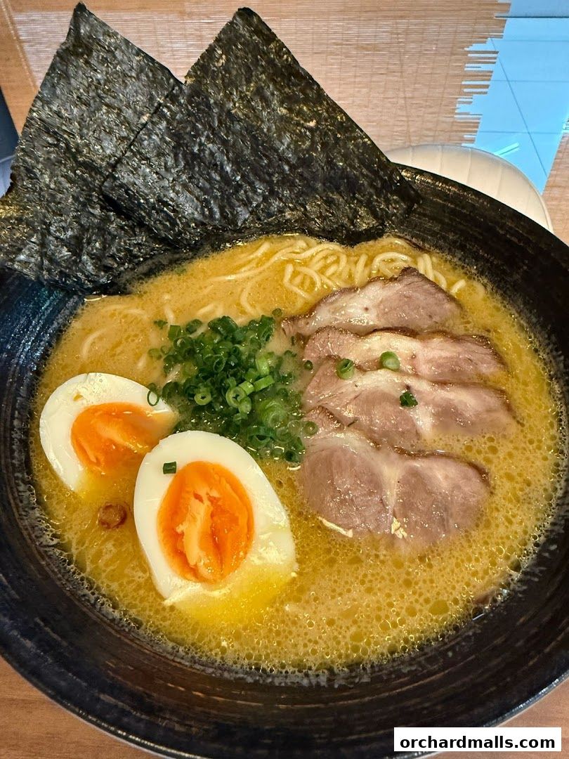 A steaming bowl of ramen with pork slices, soft-boiled eggs, and nori seaweed.