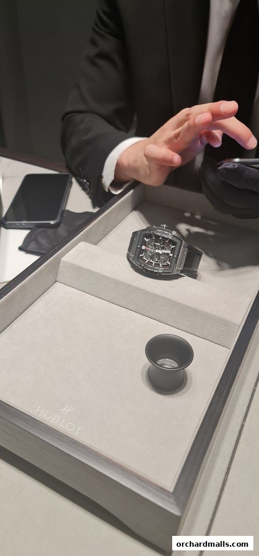 A person in a suit presents a Hublot watch in a display case.