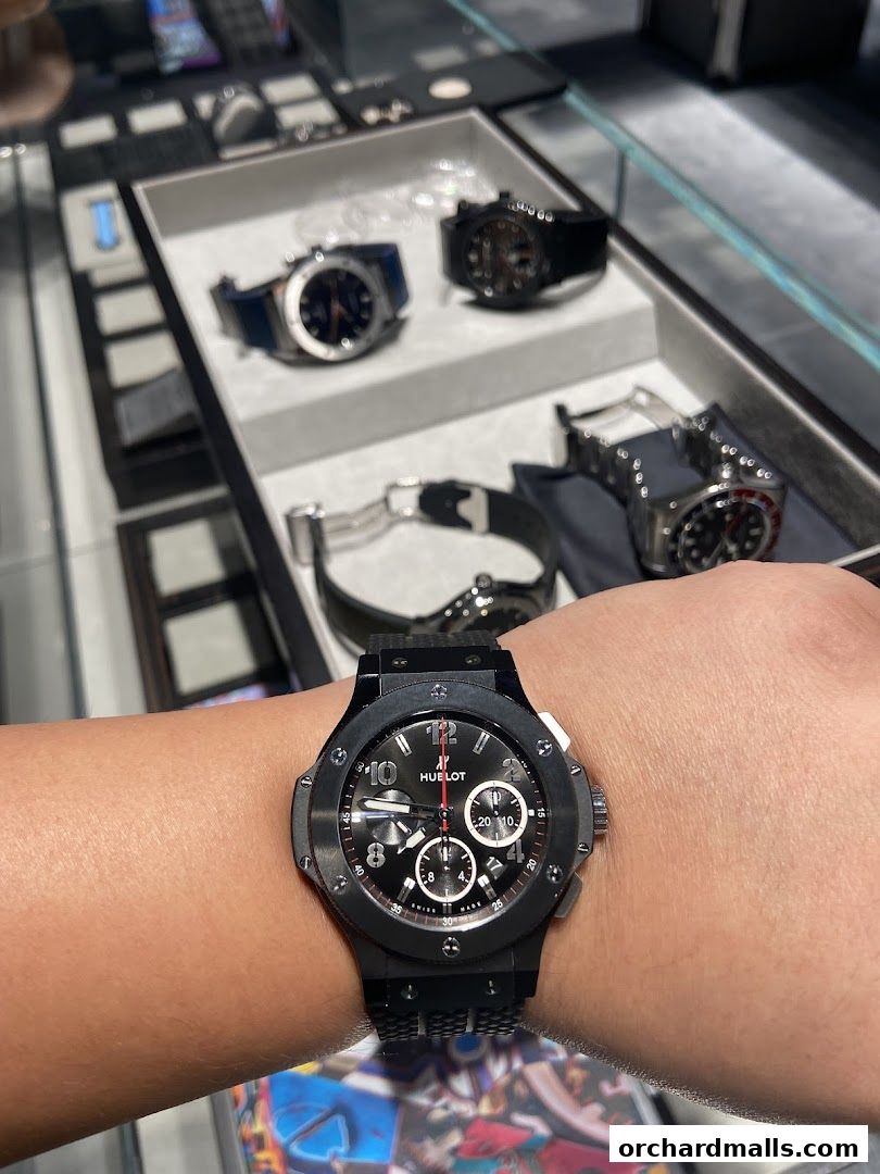 A person wearing a black Hublot watch, with other watches displayed in the background.