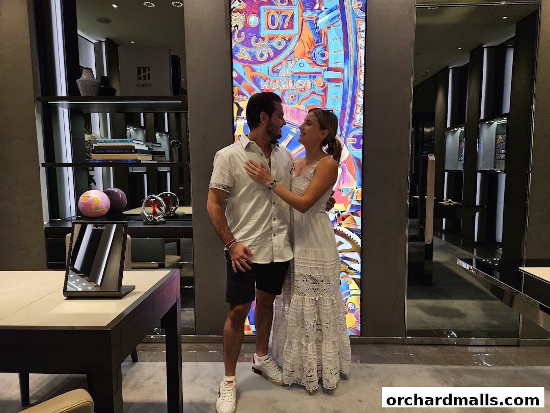 A couple poses in front of a vibrant Hublot display inside a luxury watch boutique.