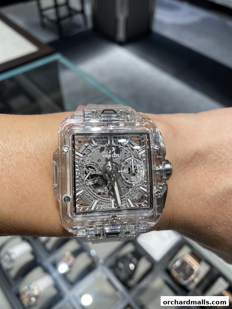 A close-up of a transparent Hublot watch on a wrist, with other watches displayed below.