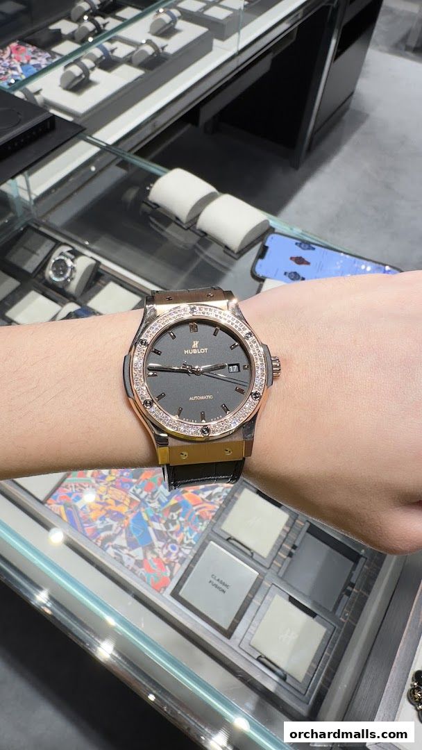 A person wearing a diamond-bezel Hublot watch with a rose gold case and black strap.