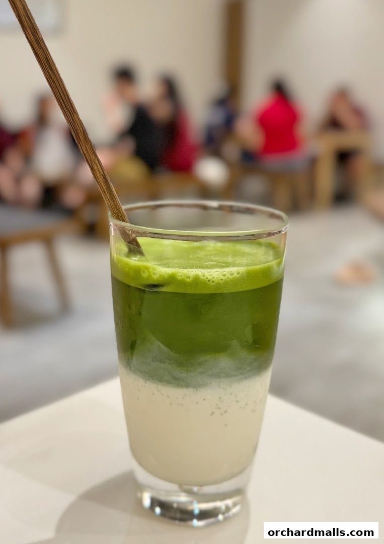 A layered matcha drink with a wooden stirrer in a clear glass.
