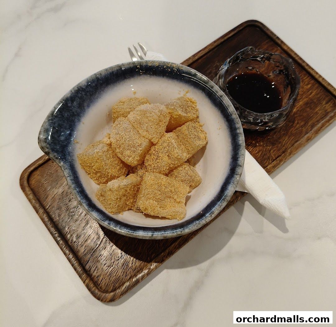 A bowl of mochi dusted with powder, served with a side of dark sauce.