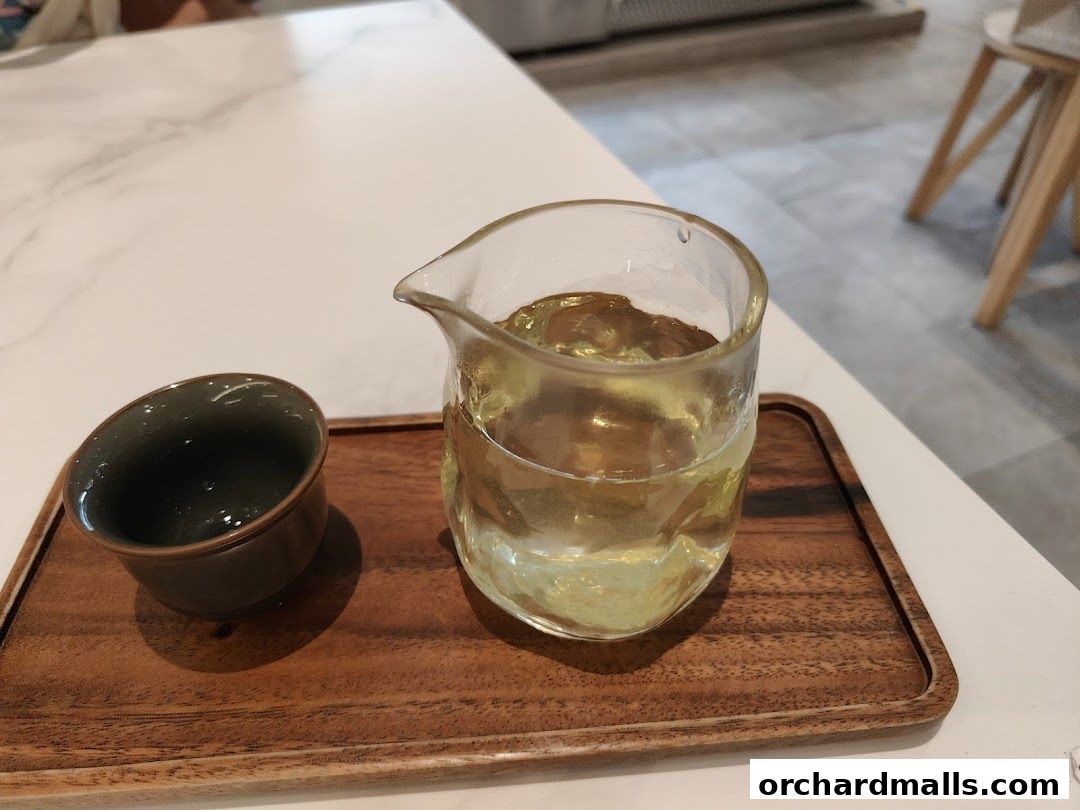 A glass pitcher of golden tea sits next to a dark teacup on a wooden tray.