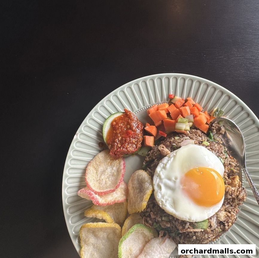A plate of nasi goreng with a fried egg, crackers, chili paste, and diced vegetables.