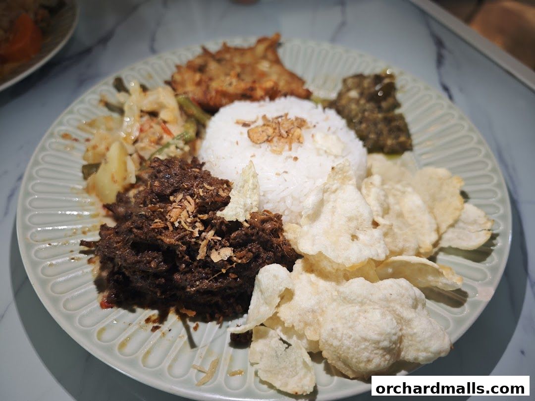 A plate of Indonesian food with rice, rendang, vegetables, and crackers.