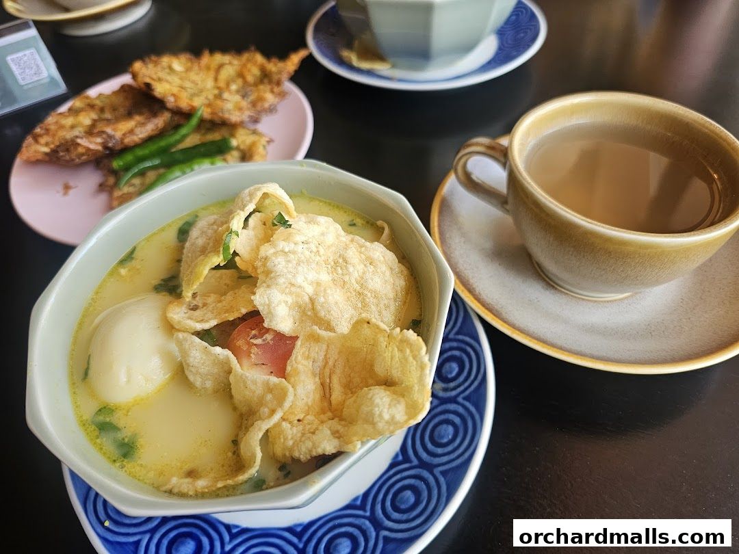 A close-up of a delicious Indonesian soup with crackers, egg, and a side of fried snacks.