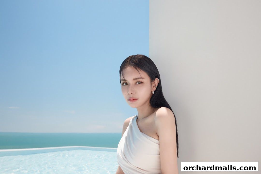 A woman with dark hair poses by a pool with a serene ocean and sky background.