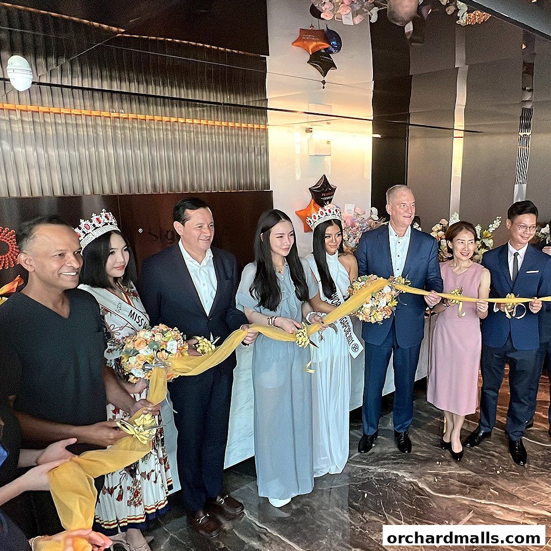 A group of people, including beauty pageant contestants, participate in a ribbon-cutting ceremony.
