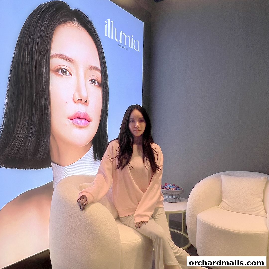 A woman sits in a modern clinic waiting area with a large illuminated advertisement behind her.