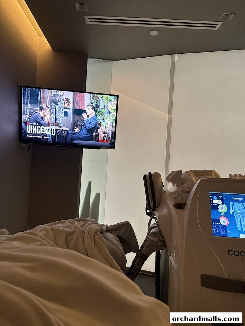 A treatment room with a bed, a TV showing a series, and a medical device.