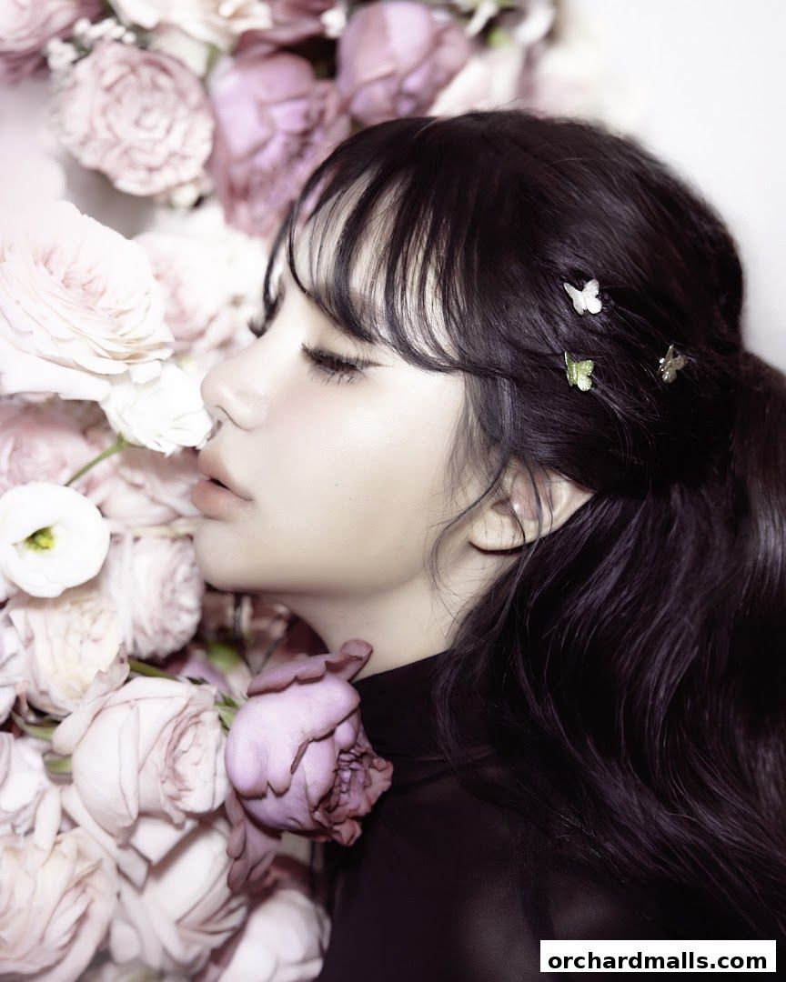 A woman with dark hair adorned with butterfly clips rests her head among pink and white roses.