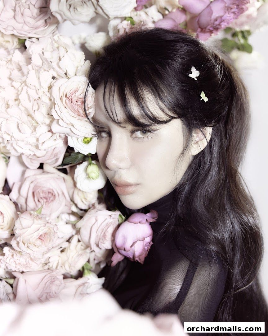 A woman with dark hair and delicate butterfly hair clips rests among soft pink and white roses.