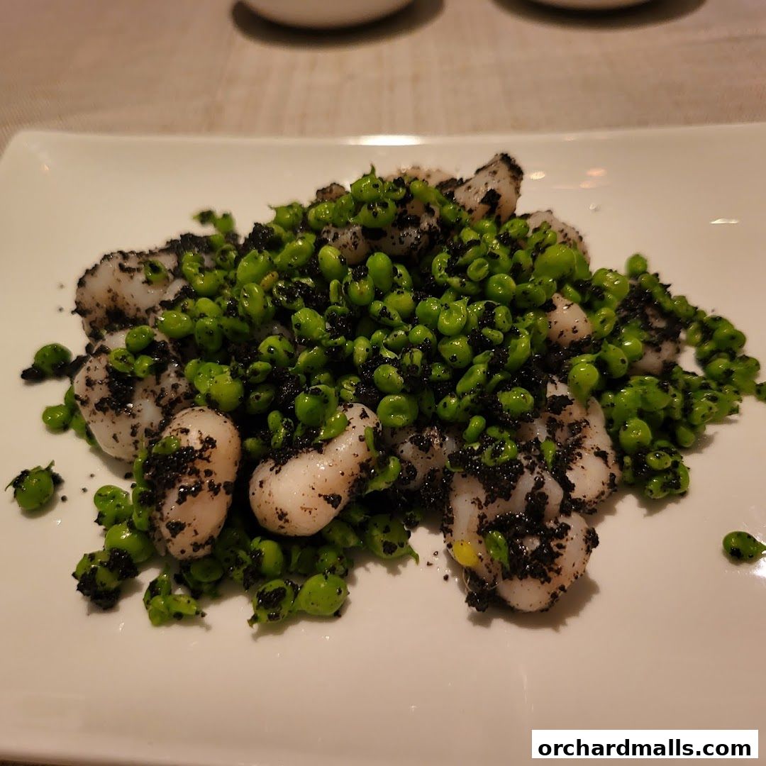 A plate of white seafood with green peas and black seasoning.