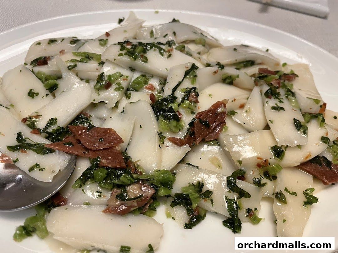 A close-up of a white plate filled with sliced white food, green herbs, and meat.