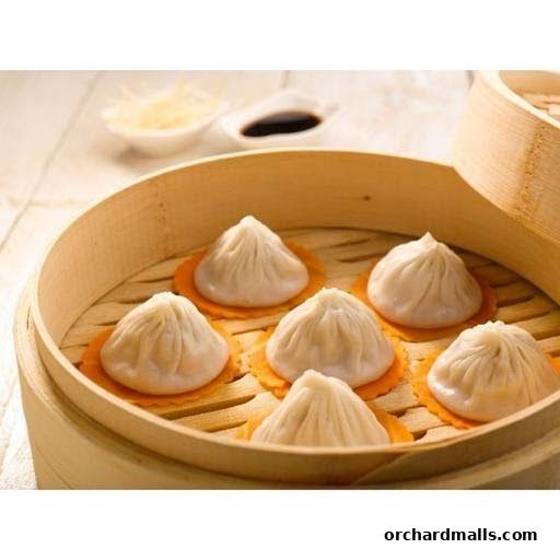 Steaming hot soup dumplings served in a bamboo steamer with dipping sauce.